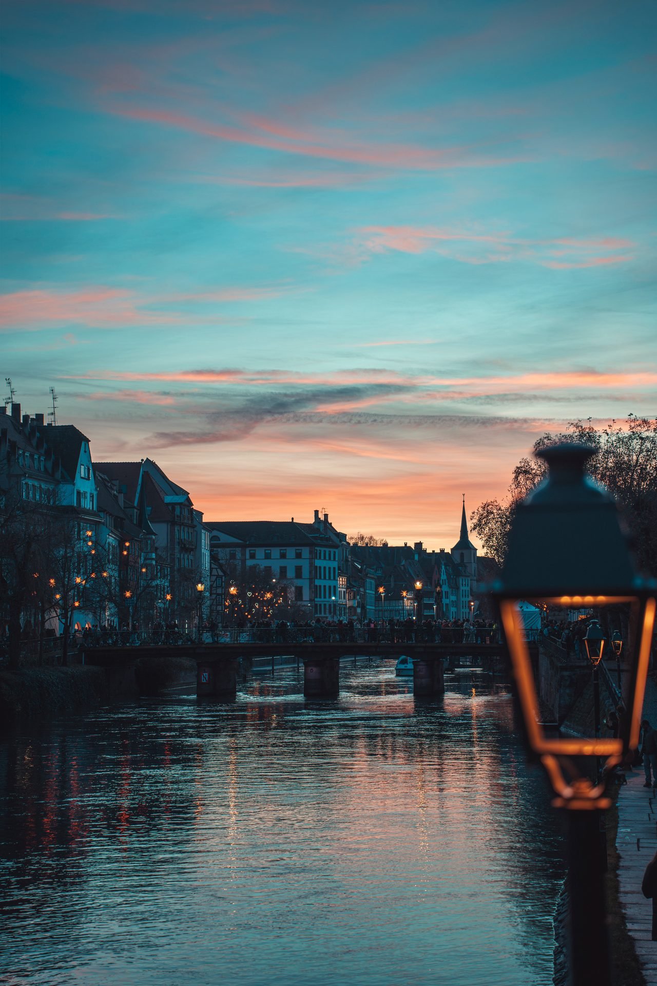 Abendhimmel über Fluss und Brücke, eine Laterne leuchtet warm