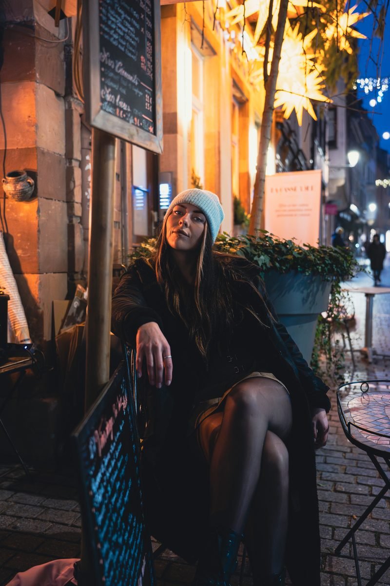 Frau mit heller Mütze sitzt abends vor einem Café neben der Tafel mit der Karte