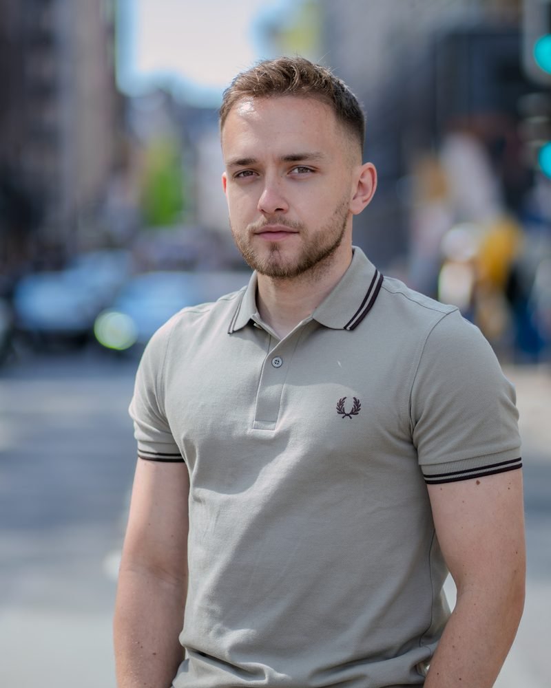 Junger Mann im hellen Poloshirt steht in einer Straße, der Hintergrund verschwimmt