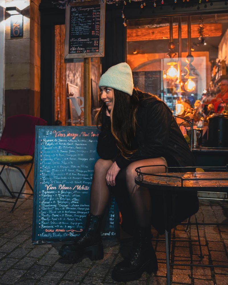 Frau sitzt abends draußen an einem Cafétisch und lächelt zur Seite